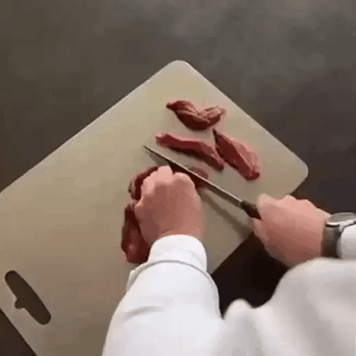 A person rinsing a titanium cutting board under running water, demonstrating its sleek, space-saving design and practicality in a modern kitchen.